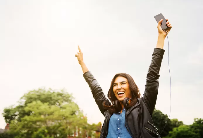 Vrouw wandelt in park en houdt beide armen omhoog met smartphone in één hand