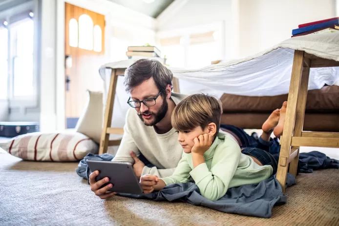 Vader en zoon liggen op tapijt en spelen een videospelletje.