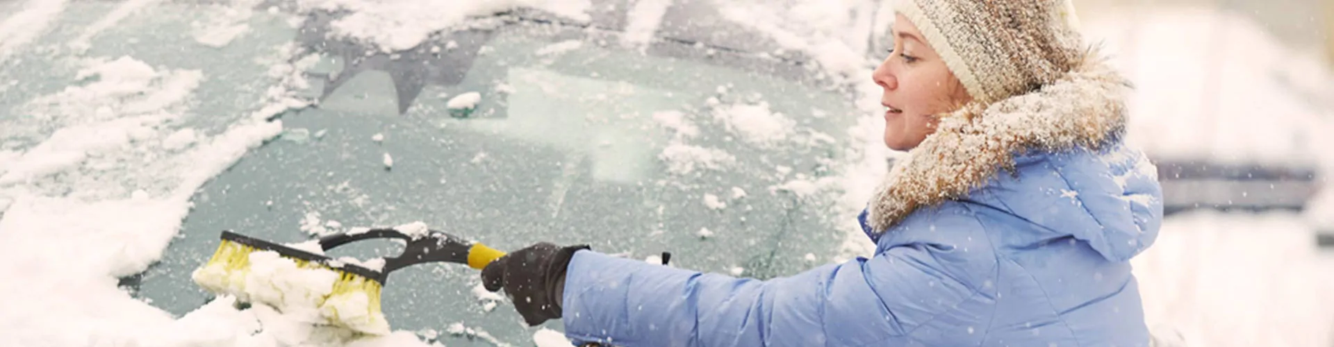 Vrouw haalt sneeuw van haar autovoorruit weg.