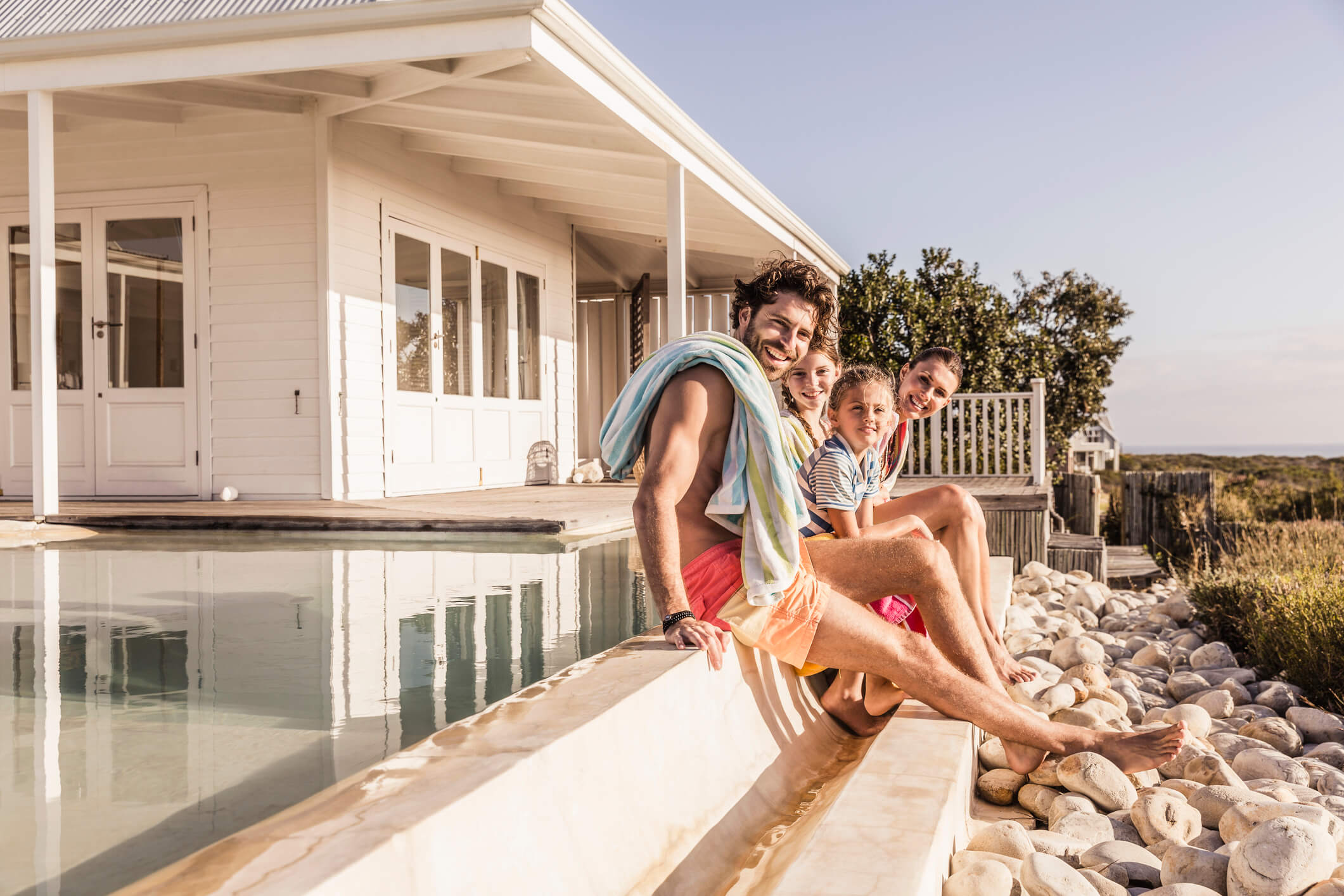 Familie zit op de rand van het zwembad van hun vakantiehuis