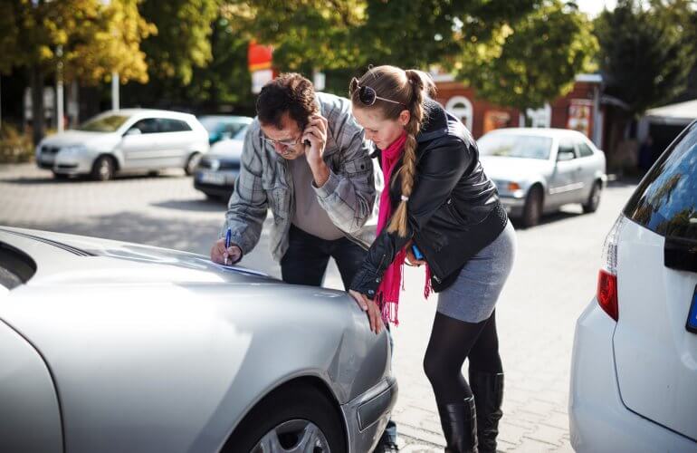 Twee mensen vullen het aanrijdingsfomulier in nadat ze met hun auto tegen elkaar gebotst zijn op een privé parking.