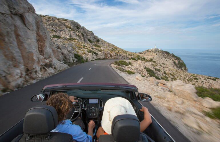 Koppel rijdt samen in cabrio langs een mooi meer op vakantie.