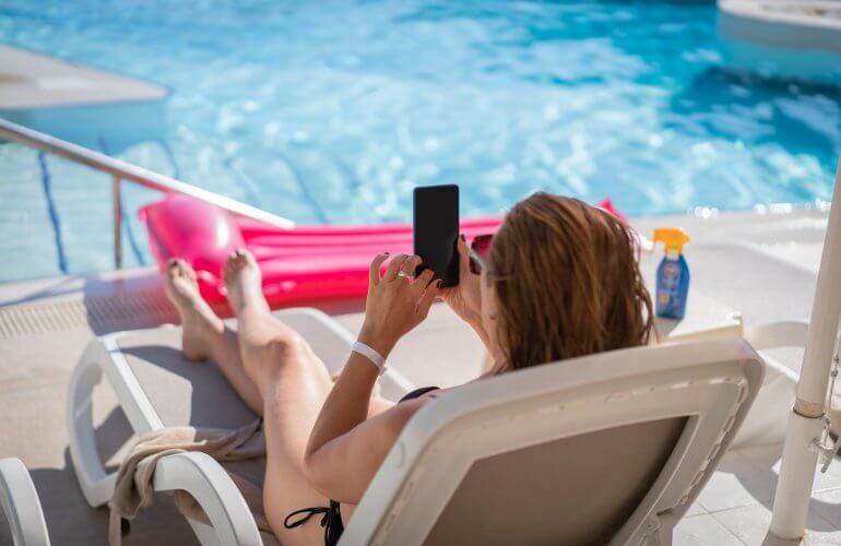 Vrouw zit met smartphone aan het zwembad.